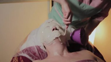 Profesyonel bir Kozmetolog yaşlı bir kadına yüz maskesi uygular. Kozkolojik yenilikler.