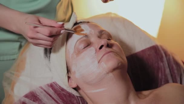 Un cosmetólogo profesional aplica una mascarilla facial a una mujer mayor. Innovaciones cosmetológicas . — Vídeos de Stock