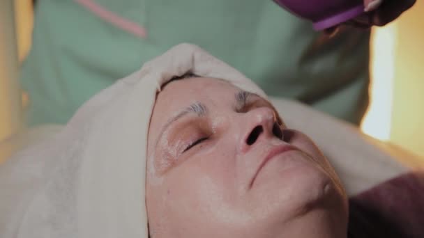 Um cosmetologista profissional aplica uma máscara facial a uma mulher idosa. Inovações cosmológicas . — Vídeo de Stock