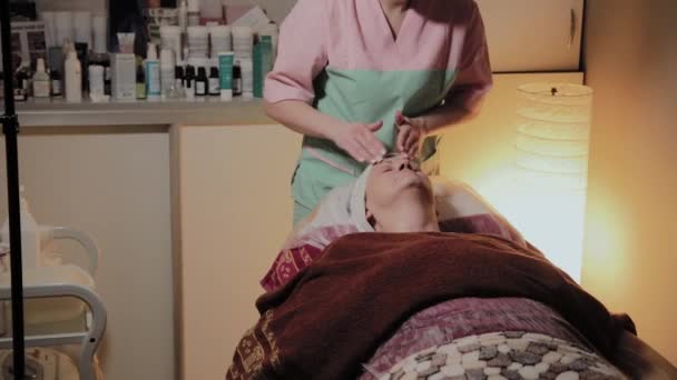 Професійний косметолог готує обличчя літньої жінки до процедури. Косметологічні інновації — стокове відео