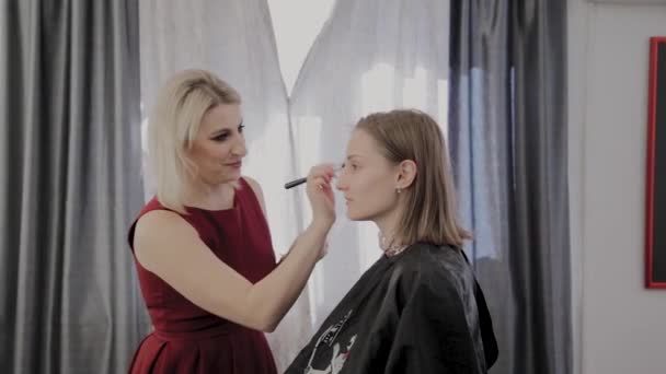Makijaż artysta stosuje profesjonalny makijaż do pięknej młodej dziewczyny. Nowa koncepcja makijażu. — Wideo stockowe
