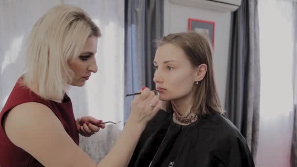 Makeup artist applicerar professionell makeup till en vacker ung flicka. Nytt koncept i makeup. — Stockvideo