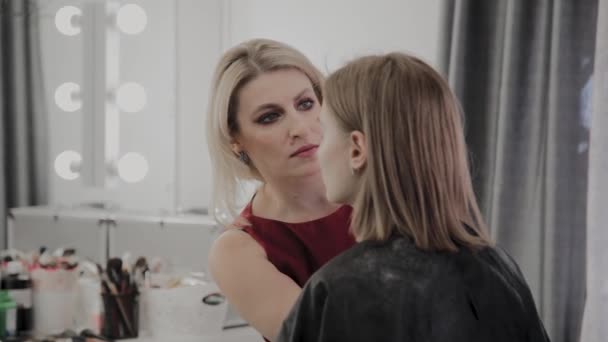 Makeup artist applicerar professionell makeup till en vacker ung flicka. Nytt koncept i makeup. — Stockvideo