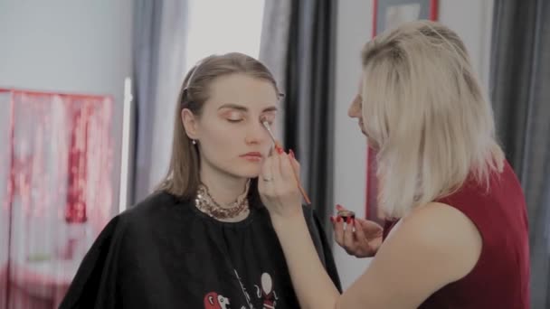 Makeup artist applicerar professionell makeup till en vacker ung flicka. Nytt koncept i makeup. — Stockvideo