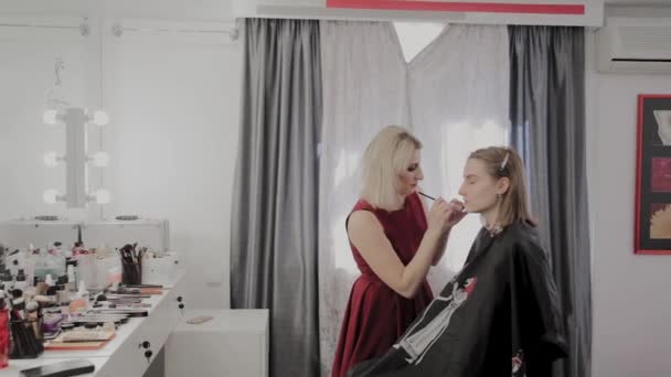 Makeup artist applicerar professionell makeup till en vacker ung flicka. Nytt koncept i makeup. — Stockvideo