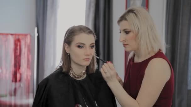 Makeup artist applicerar professionell makeup till en vacker ung flicka. Nytt koncept i makeup. — Stockvideo