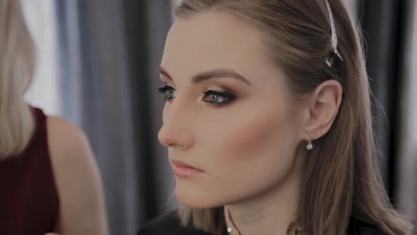Maquillaje artista aplica maquillaje profesional a una hermosa joven. Nuevo concepto en maquillaje . — Vídeos de Stock
