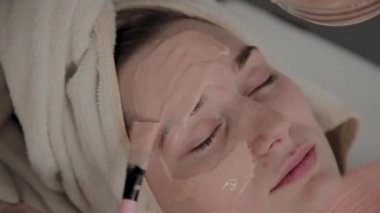 Profesyonel bir Kozmetolog bir fırça ile genç bir kıza bir yüz maskesi uygular. Kozmetolojide yeni konsept.