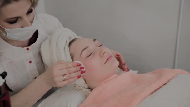 Um cosmetologista profissional esfrega o rosto das meninas com toalhetes hidratantes especiais. Novo conceito em cosmetologia . — Vídeo de Stock