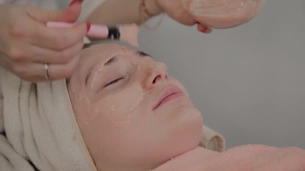 Un cosmétologue professionnel applique un masque facial à une jeune fille avec un pinceau. Nouveau concept en cosmétologie . — Video