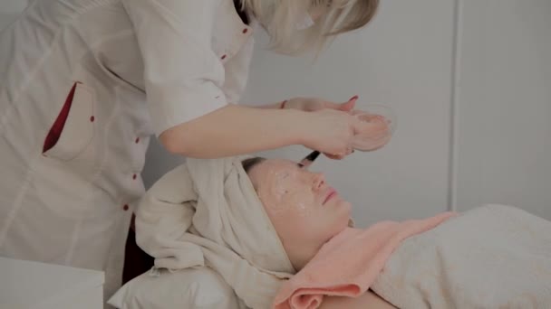 Un cosmetologo professionista applica una maschera per il viso a una giovane ragazza con un pennello. Nuovo concetto in cosmetologia . — Video Stock