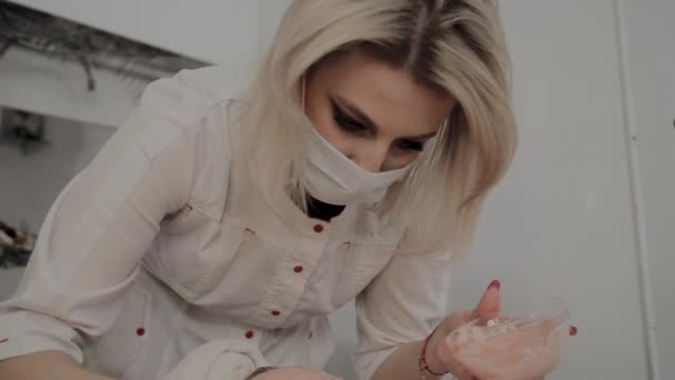 Um cosmetologista profissional aplica uma máscara facial a uma jovem com um pincel. Novo conceito em cosmetologia . — Vídeo de Stock