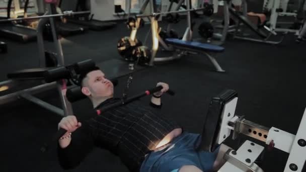 Wesoły gruby człowiek wykonuje złe ćwiczenia w siłowni. Po raz pierwszy w klubie fitness. — Wideo stockowe