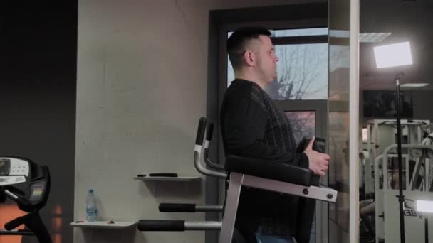 Hombre gordo alegre realiza un ejercicio equivocado en el gimnasio. Por primera vez en un gimnasio . — Vídeo de stock