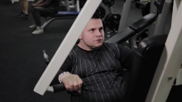 Веселый толстяк выполняет неправильные упражнения в тренажерном зале. Впервые в фитнес-клубе . — стоковое видео