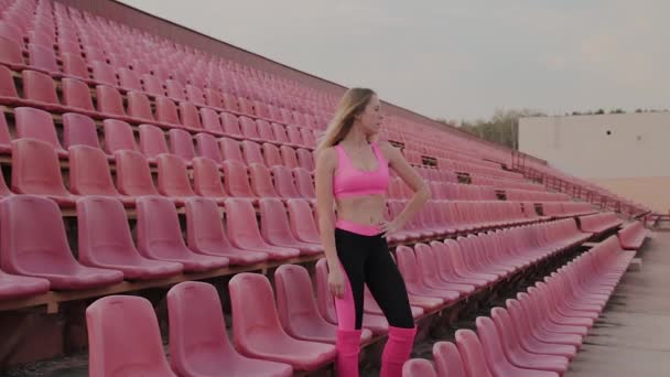 La chica está de pie junto a los asientos en el estadio, descansar después de una carrera . — Vídeos de Stock
