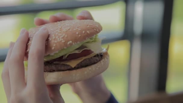 Schönes Mädchen mit einem Burger in der Hand. Fast-Food-Restaurant. — Stockvideo