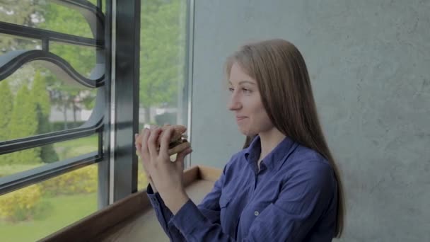 Hermosa chica sosteniendo una hamburguesa en sus manos. Restaurante de comida rápida . — Vídeos de Stock