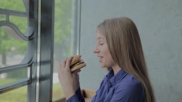 Mooi meisje houdt een hamburger in haar handen. Fast Food Restaurant. — Stockvideo