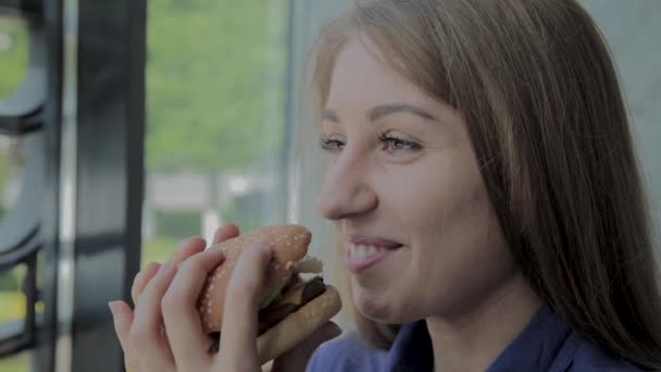 Hermosa chica come una hamburguesa. Restaurante de comida rápida — Vídeos de Stock