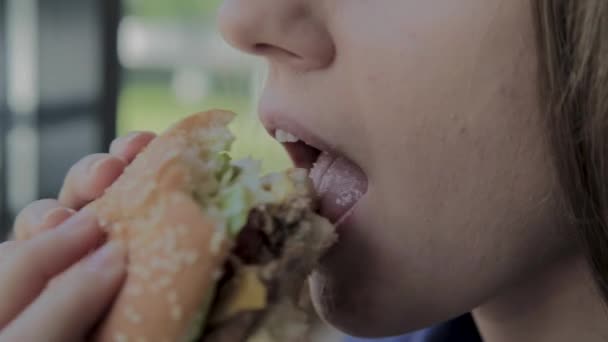 Hermosa chica come una hamburguesa. Restaurante de comida rápida — Vídeos de Stock