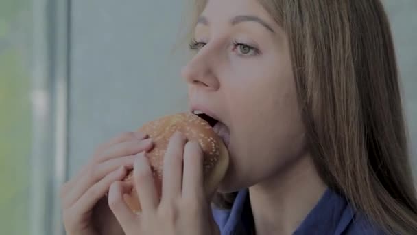 Το όμορφο κορίτσι τρώει ένα μπέργκερ. Φαστ φουντ εστιατόριο — Αρχείο Βίντεο