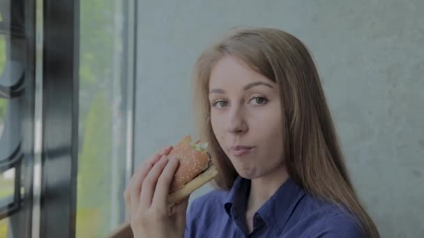 Hermosa chica come una hamburguesa. Restaurante de comida rápida — Vídeos de Stock