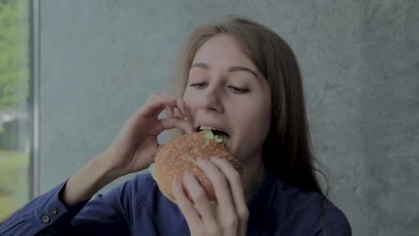 Beautiful girl eats a burger. Fast food restaurant — Stock Video