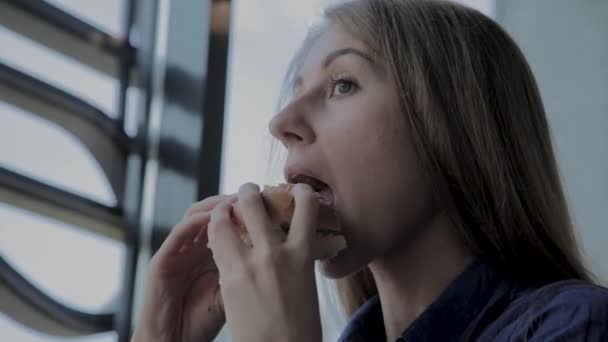 Hermosa chica come una hamburguesa. Restaurante de comida rápida — Vídeo de stock