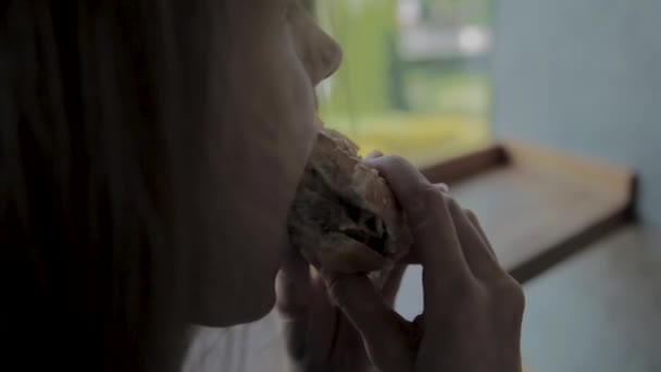 Vacker flicka äter en hamburgare. Snabbmatsrestaurang — Stockvideo