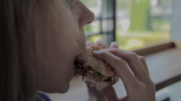 Hermosa chica come una hamburguesa. Restaurante de comida rápida — Vídeo de stock