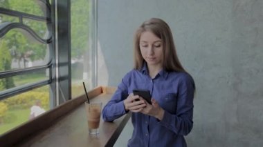 Bir kafede bir telefon ile pencerede oturan güzel kız.