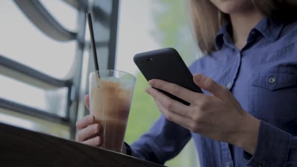 Hermosa chica sentada junto a la ventana con un teléfono en un café . — Vídeo de stock