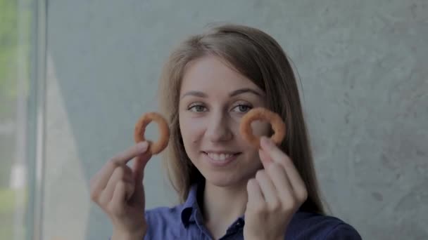 A menina traz anéis de cebola para o rosto e sorri em um restaurante de fast-food . — Vídeo de Stock