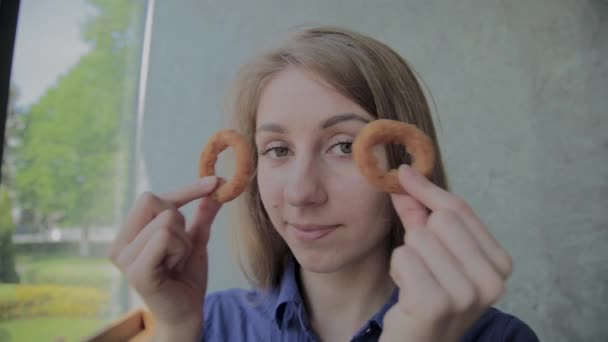 Het meisje brengt uienringen naar haar gezicht en glimlacht in een fast-food restaurant. — Stockvideo