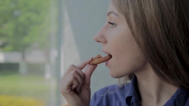 Chica come aros de cebolla y sonríe en un restaurante de comida rápida . — Vídeos de Stock