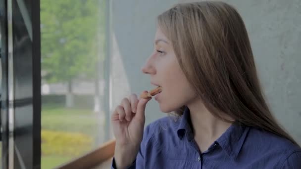 Chica come aros de cebolla y sonríe en un restaurante de comida rápida . — Vídeo de stock