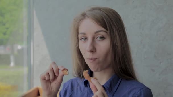 Meisje eet uienringen en glimlacht in een fast food restaurant. — Stockvideo