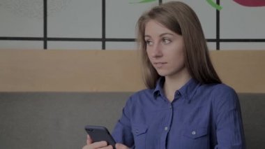 Güzel bir kız bir kafede bir telefon ve içme kahve ile oturuyor.