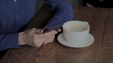 Güzel bir kız bir kafede bir telefon ve içme kahve ile oturuyor.