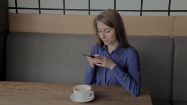 Güzel bir kız bir telefon ile bir kafede oturur ve onun kahve resimleri alır.