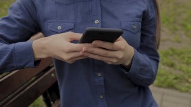 Bir cep telefonu ile bir şehir parkında bir bankta oturan güzel mutlu kız.