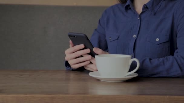 Una hermosa chica está sentada en un café con un teléfono y tomando café . — Vídeo de stock