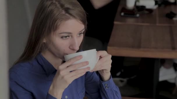 Une belle fille est assise dans un café et boit du café . — Video