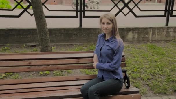 Belle fille assise sur un banc dans un parc de la ville . — Video