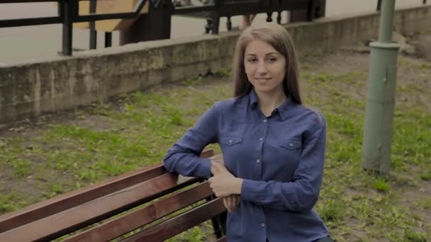 Vacker flicka sitter på en bänk i en stads Park. — Stockvideo