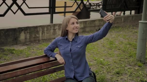 Hermosa chica feliz haciendo selfie en el parque en un banco . — Vídeo de stock
