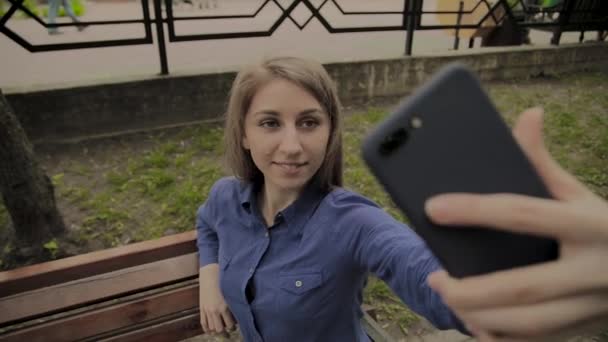 Schönes glückliches Mädchen macht Selfie im Park auf einer Bank. — Stockvideo