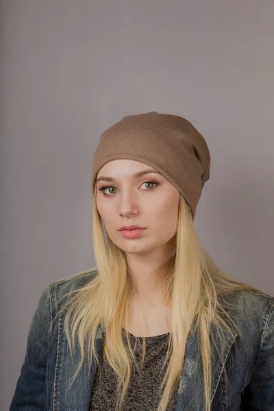 Portret van een mooi jong meisje in een stijlvolle hoofdtooi met natuurlijke make-up op een grijze achtergrond. — Stockfoto