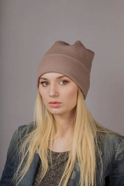 Portret van een mooi jong meisje in een stijlvolle hoofdtooi met natuurlijke make-up op een grijze achtergrond. — Stockfoto